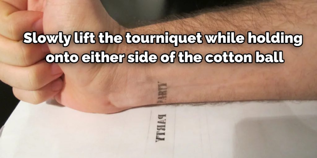 slowly lift the tourniquet while holding onto either side of the cotton ball