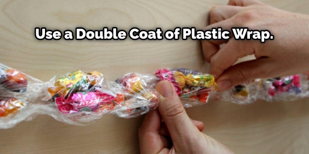 Take the outer side now and bring it back towards the middle, so that around the sweets, you use a double coat of plastic wrap.